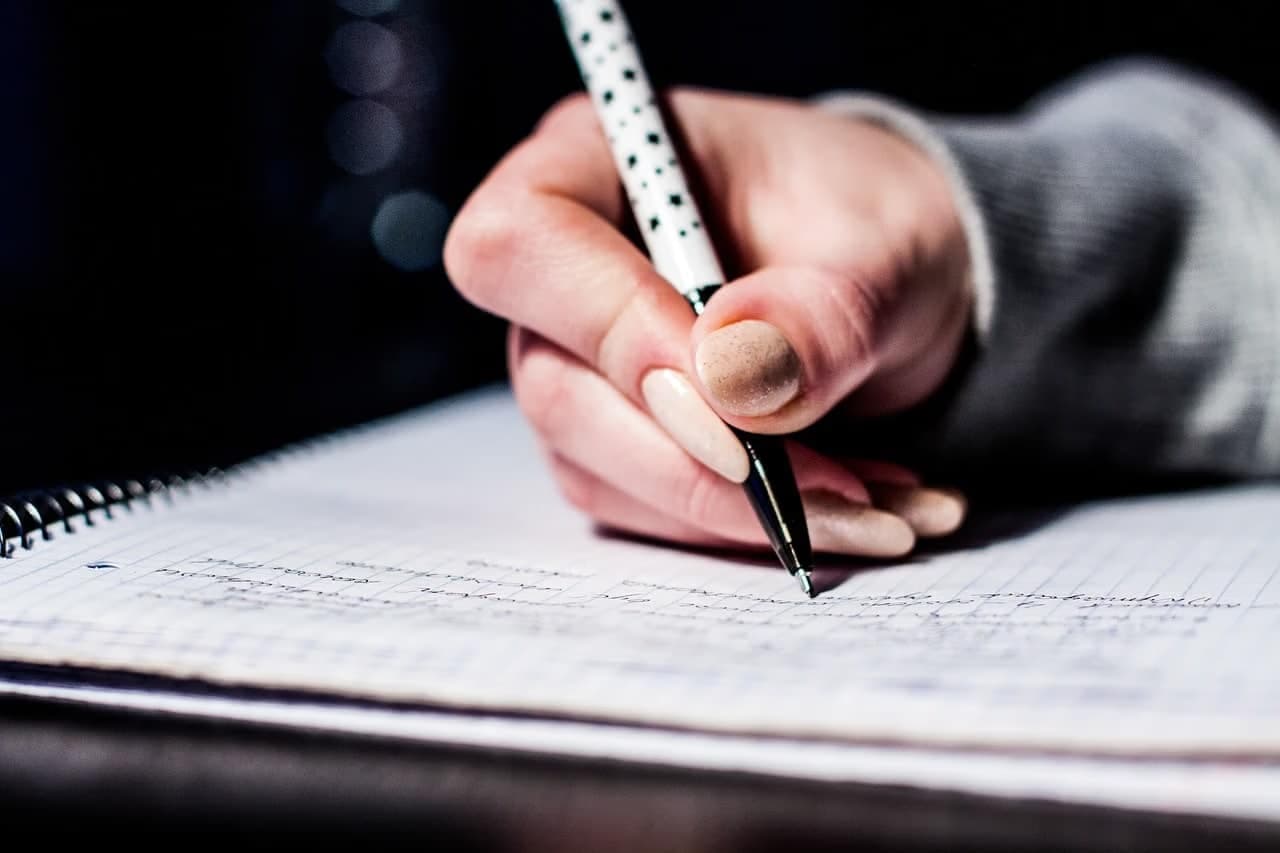 A close-up of a hand writing notes on a page in a spiral notebook.